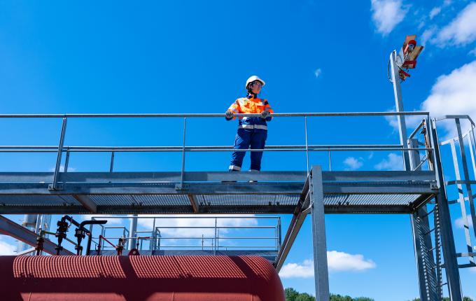 photo of a Storengy employee wearing safety equipment on a storage site. He is at the top of an installation and the photo is taken from the back.