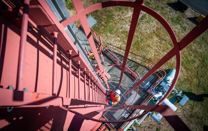 photo of a Storengy employee in safety equipment. He is climbing the ladder of a processing tower. The photo is taken from above. 