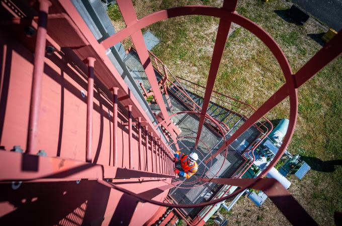 photo of a Storengy employee in safety equipment. He is climbing the ladder of a processing tower. The photo is taken from above. 